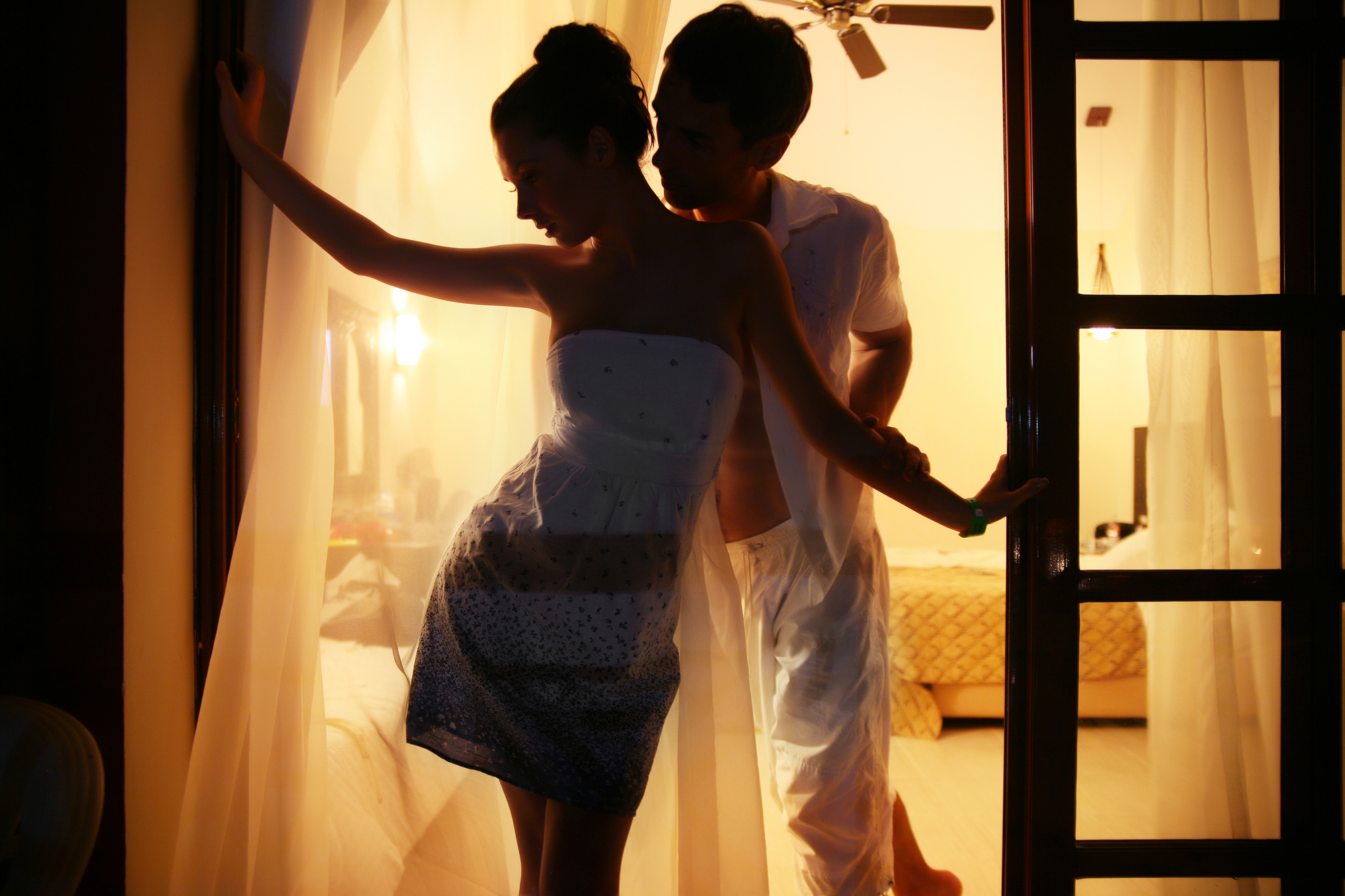 sexy date ideas - image of couple standing in front of open balcony door, lit from behind with golden yellow glow