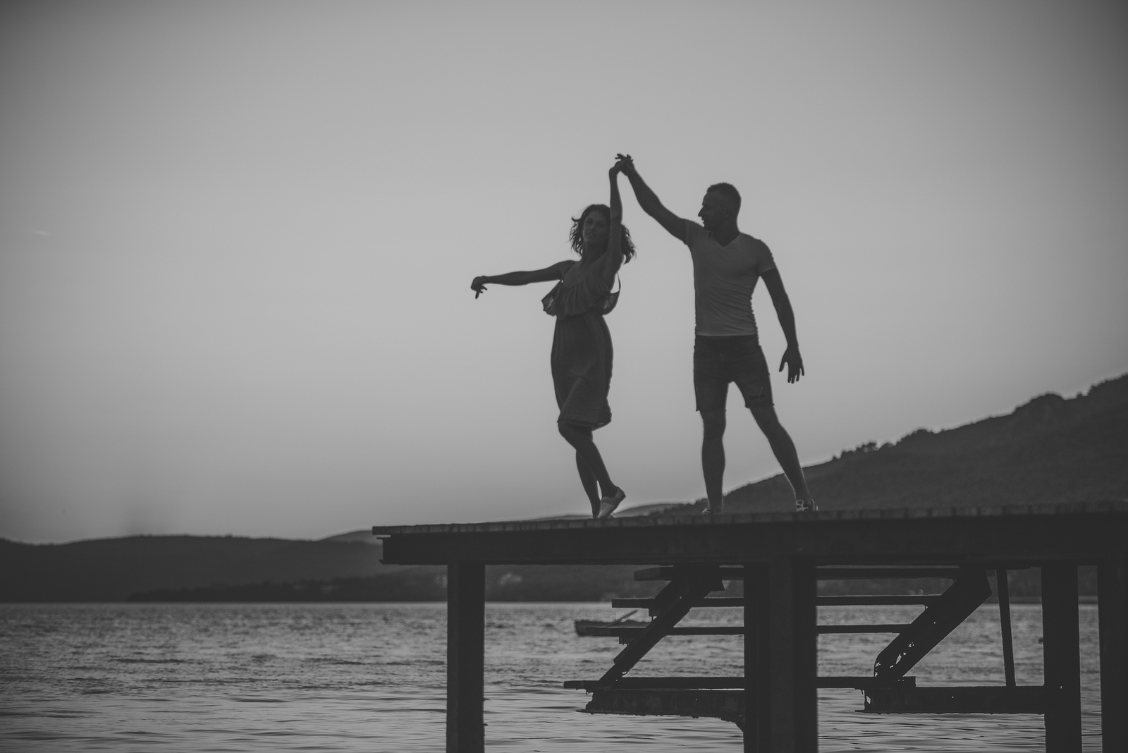 instagram captions for couples - Romance and love concept. Silhouette of sensual couple dancing on pier with sunset above sea surface on background. Couple in love on romantic date in evening at dock