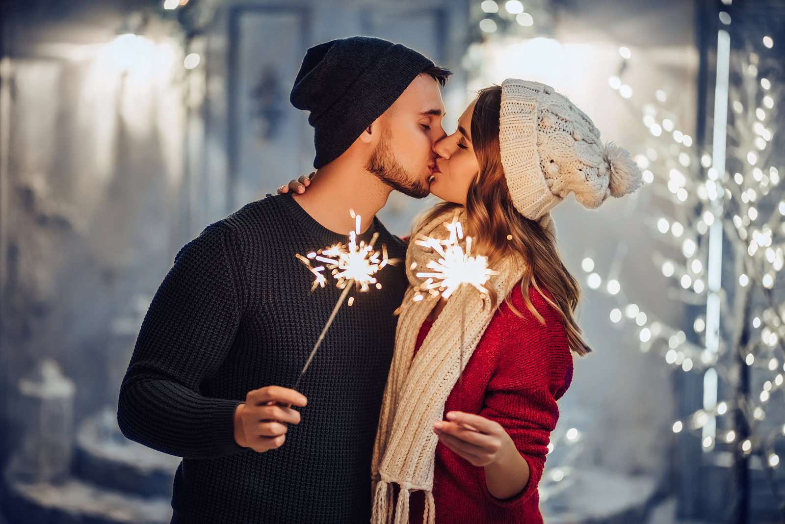 Christmas traditions for couples - couple outside in winter clothes kissing and holding lit sparklers