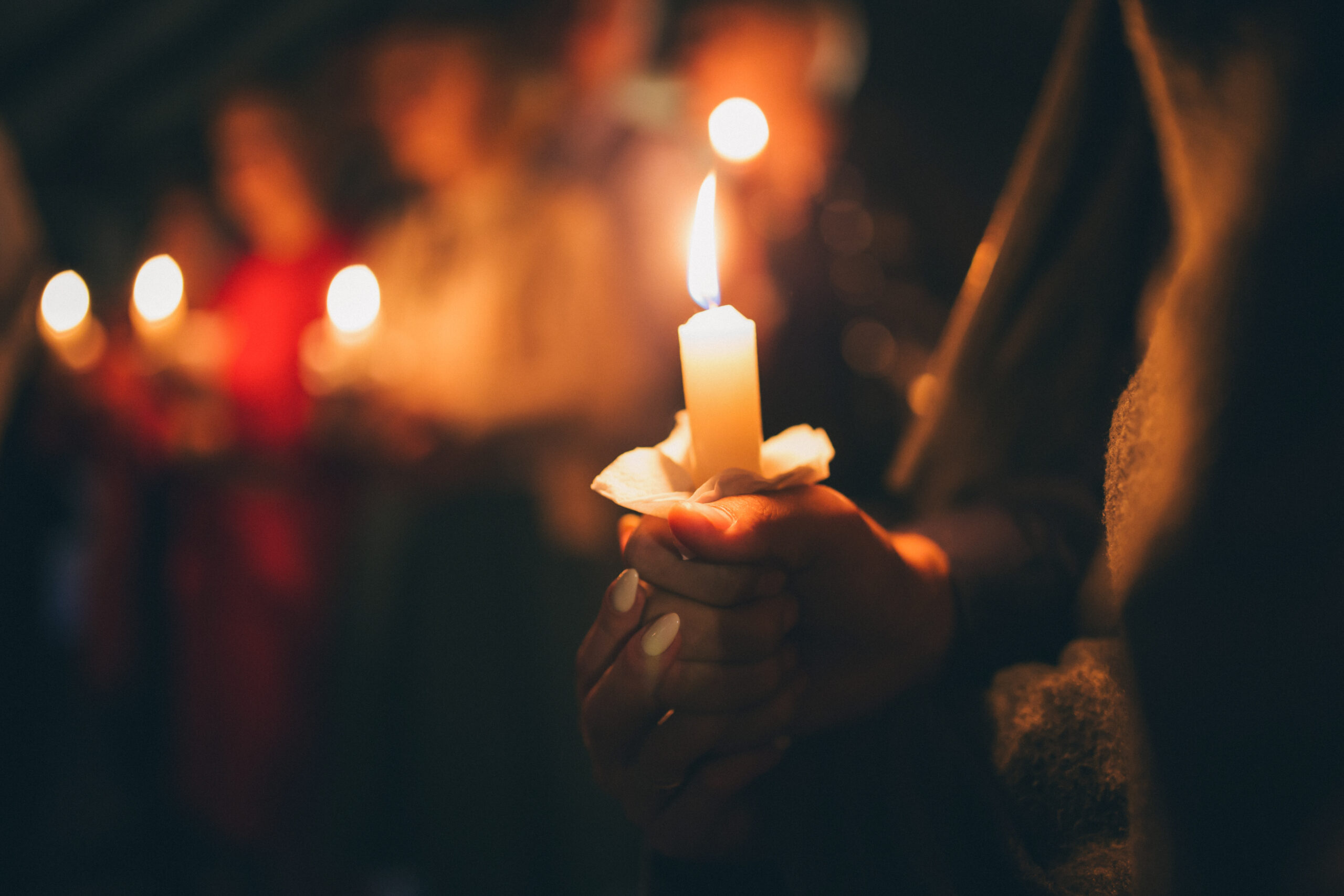 converting to catholicism - image of candles burning against dark background, hands holding lit candles