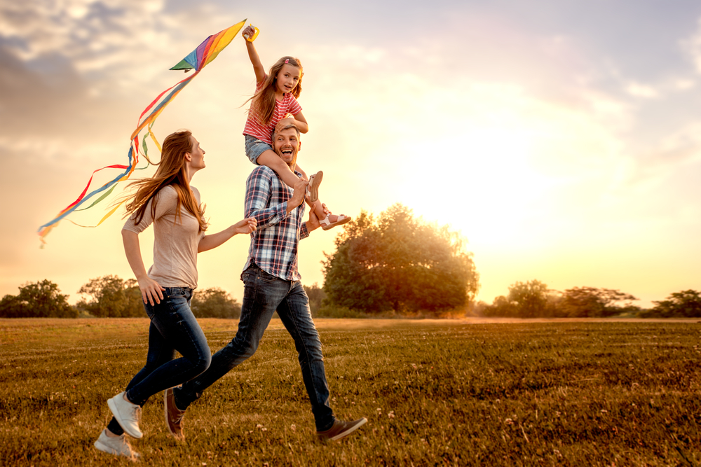 family running outside at sunset with a kite