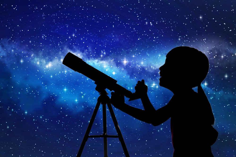 Girl using a microscope surrounded by a sky of stars