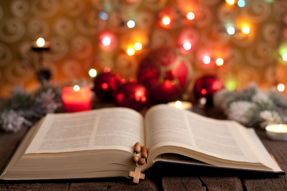 an open bible sits in front of a bright christmas scene with lights and ornaments