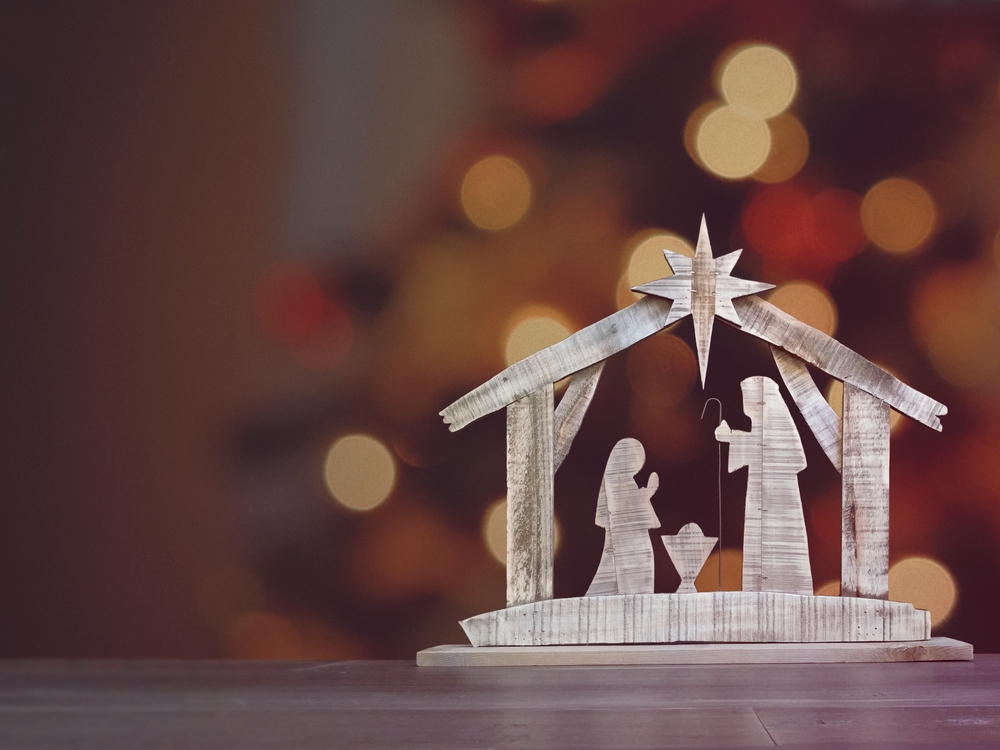 a wooden christmas nativity seen in front of a blurry christmas tree